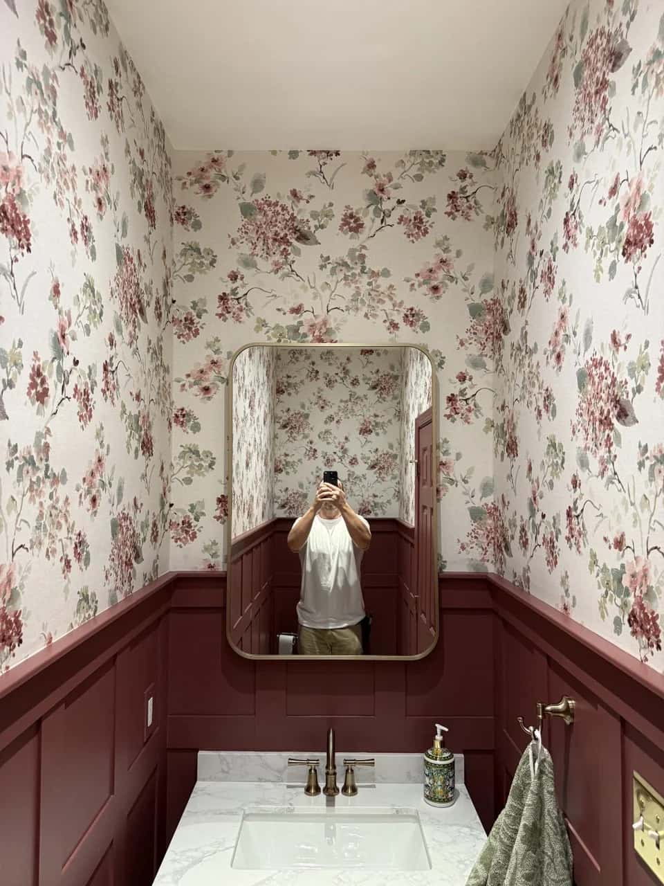Floral wallpaper above deep red wainscot in a powder room