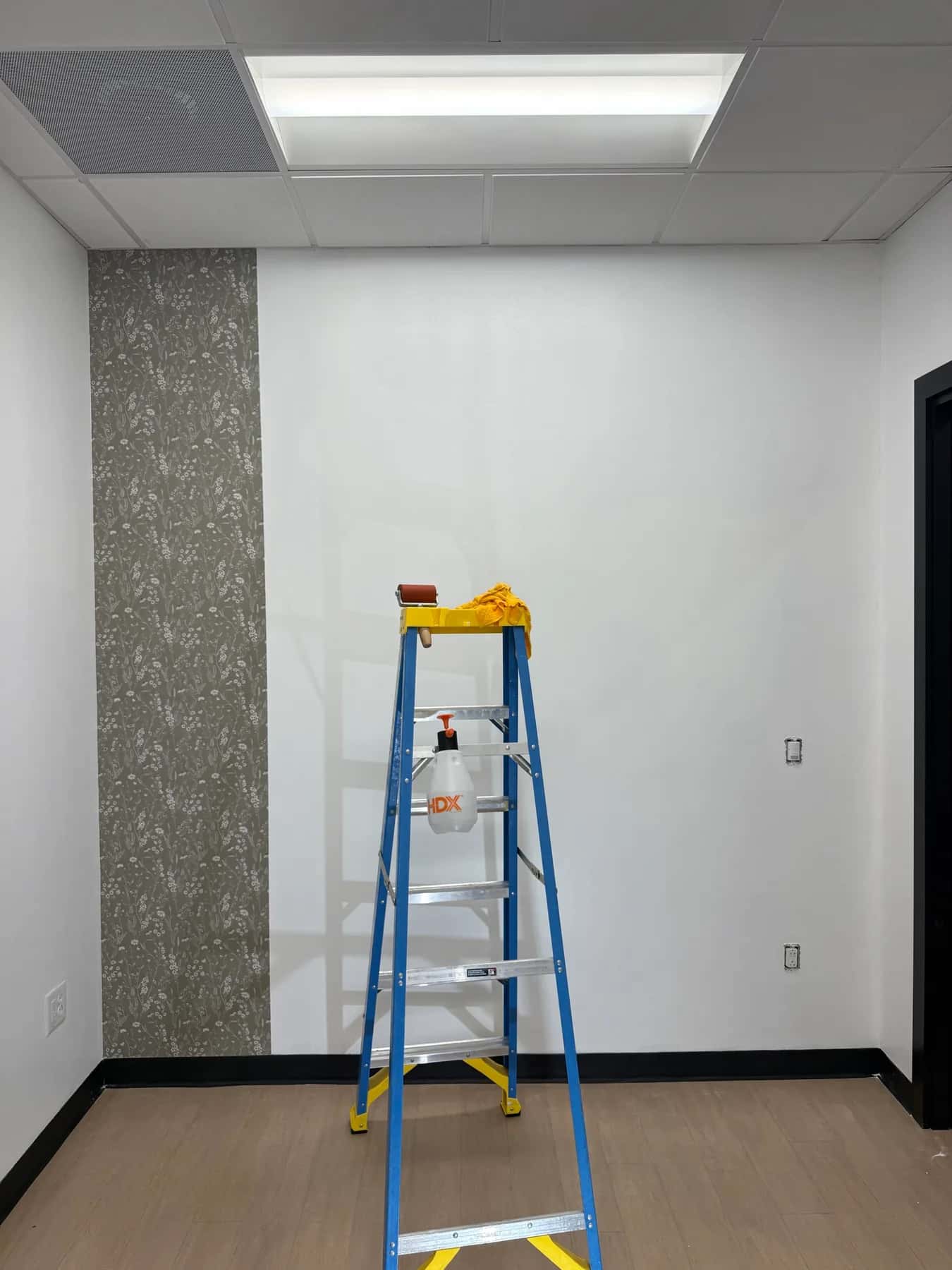 First strip of sage green wildflower peel-and-stick wallpaper at the left edge of the wall