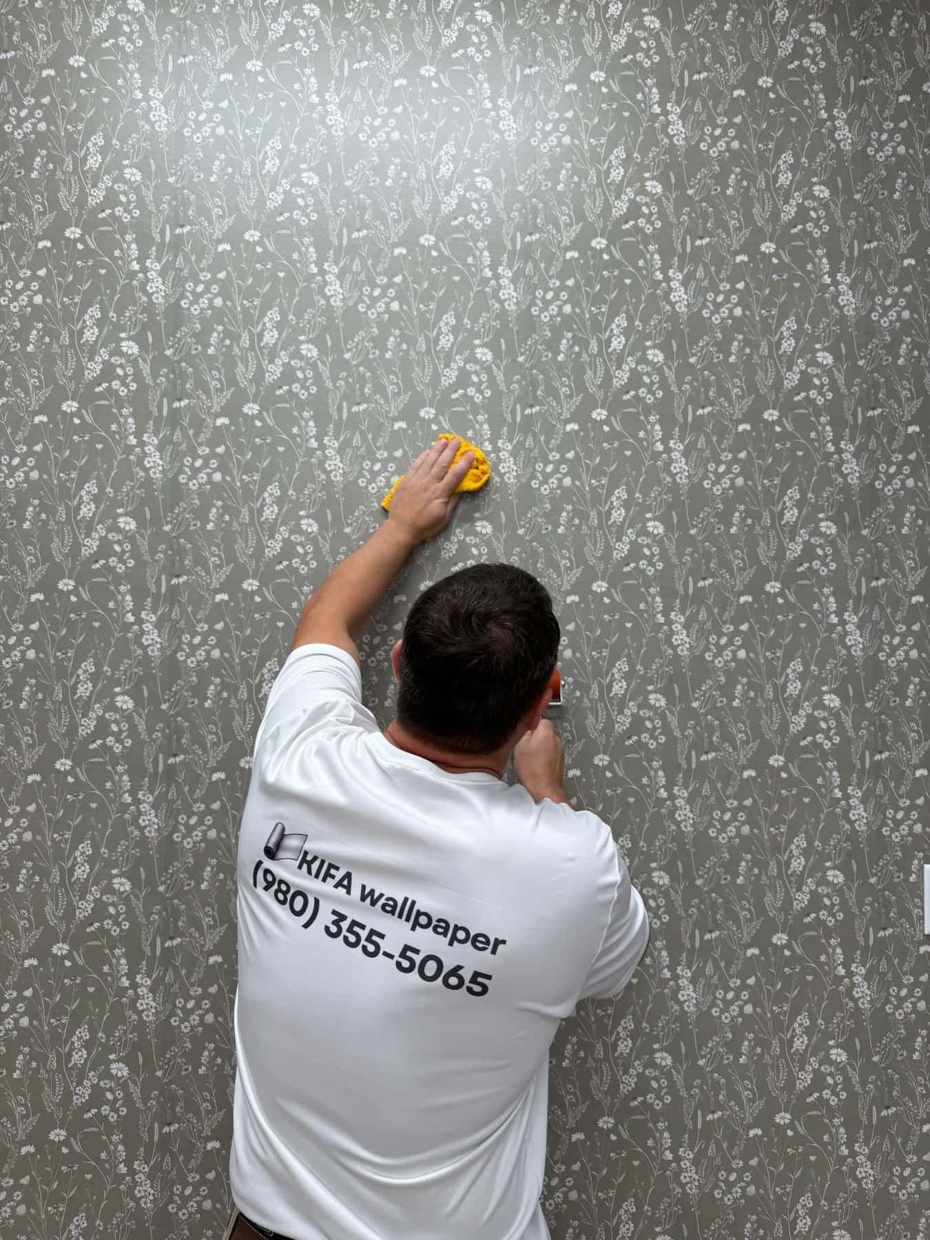 Alex smoothing a strip of wildflower peel-and-stick wallpaper with a sponge