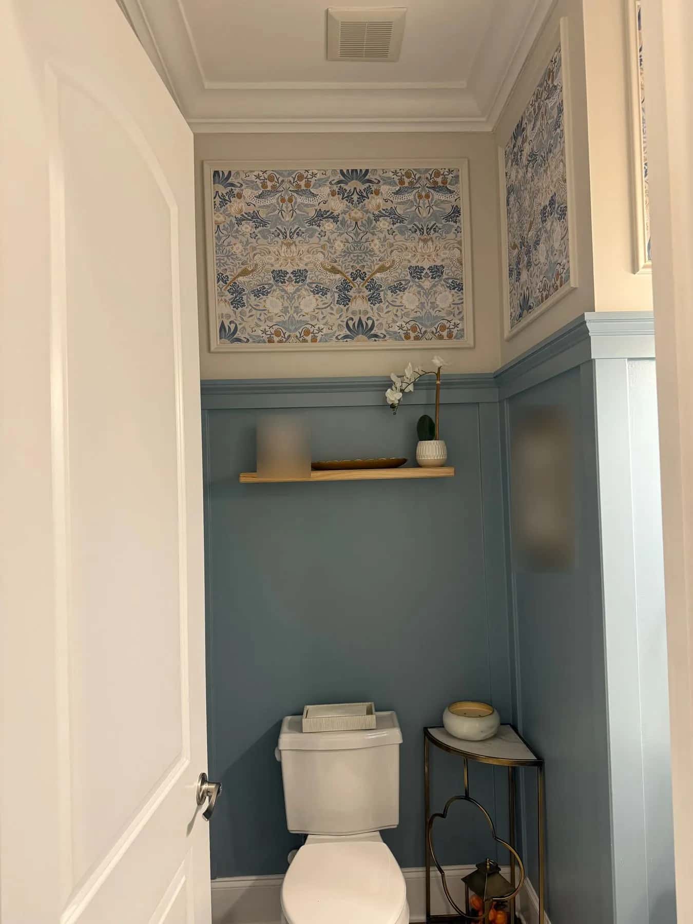 Patterned wallpaper panels in molding frames above blue wainscot and a floating shelf