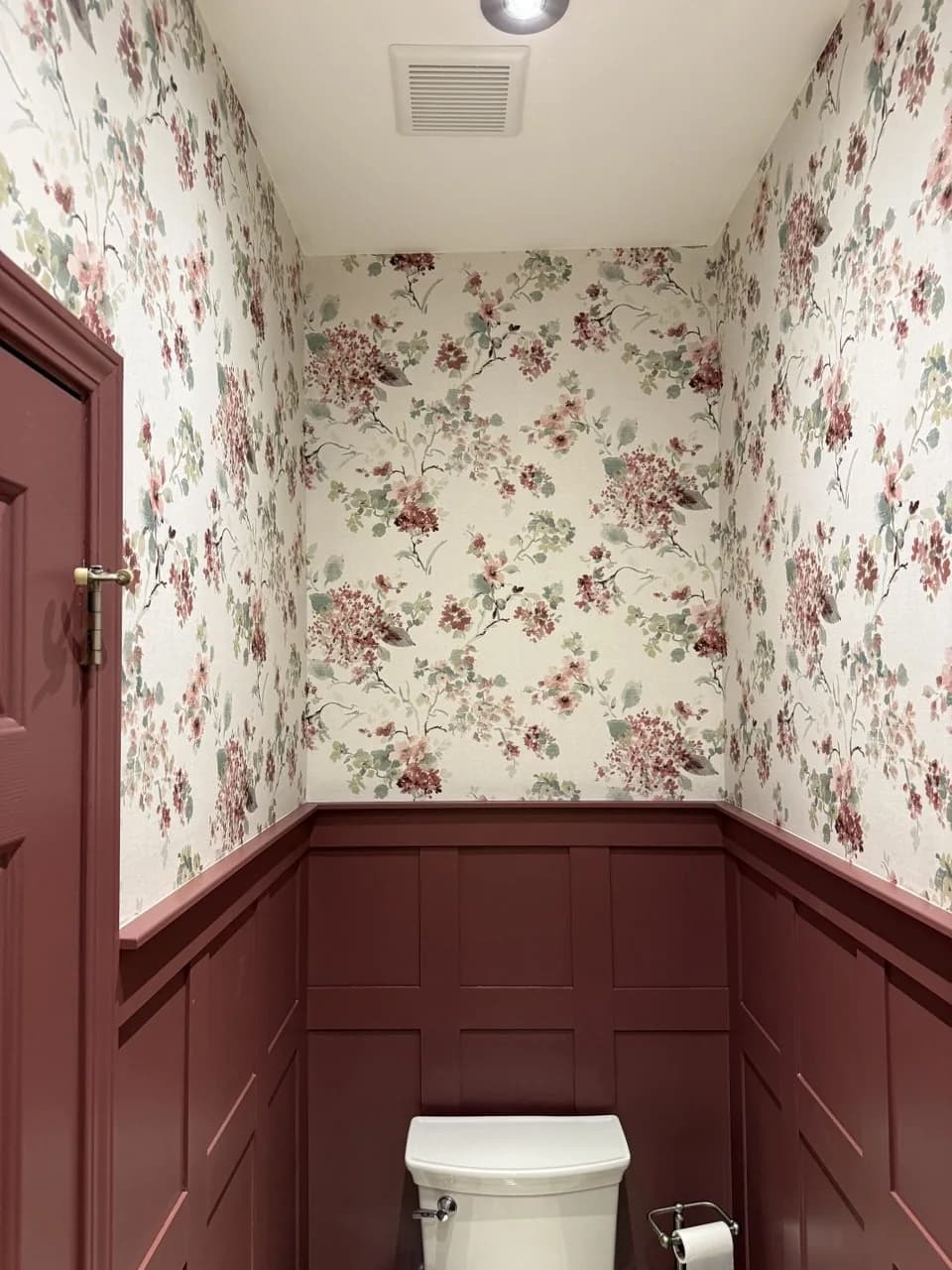 The same powder room after, floral wallpaper above the wainscot