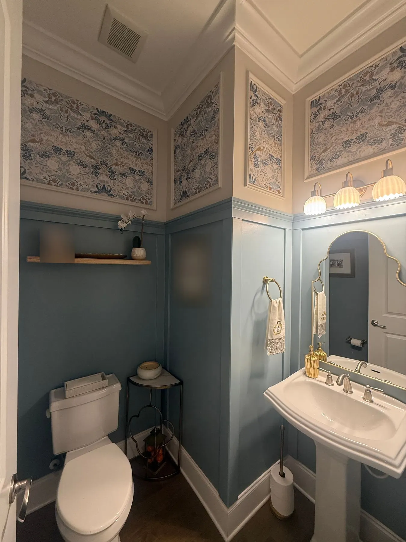Charlotte powder room with blue and cream patterned wallpaper inside picture frame molding above blue wainscot